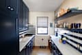 Navy blue kitchen cabinets with white marble countertops, striped window shade, and decorative dishware on shelves.