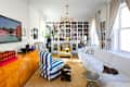 Bright living room featuring a white sectional sofa, striped chair, yellow accent chair, and a bookshelf filled with books.