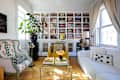 Cozy living room with a bookshelf, yellow armchair, floral-patterned chair, white sofa, and a glass coffee table.