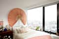 Large fan over neatly made bed in bedroom over looking cityscape.