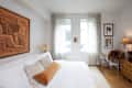 Cozy bedroom featuring a white bed with decorative pillows, a large artwork, and a wooden desk with a chair.