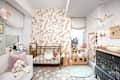 Cozy nursery with floral wallpaper, a wooden crib, plush toys, and a changing table, featuring soft pastel colors.