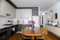 Modern kitchen with dark and light cabinetry, a wooden dining table, yellow chairs, and a vase of pink flowers.