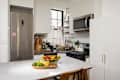 Bright kitchen featuring a stainless steel fridge, white cabinets, and a fruit bowl with bananas, limes, and apples.