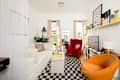 Cozy living room with a white sofa, red armchair, orange accent chair, and a checkered rug. Shelves display books and decor.