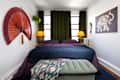Cozy bedroom featuring a purple bedspread, green curtains, decorative fan, and an elephant artwork.