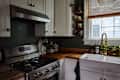Modern kitchen with stainless steel appliances, wooden countertops, white cabinets, and decorative plants on shelves.