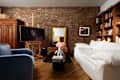Cozy living room with exposed brick walls, a white sofa, blue armchair, and a black coffee table with flowers.