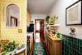 Narrow kitchen hallway with yellow patterned wallpaper, wooden cabinets, green tile backsplash, and plants on shelves.