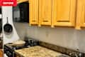 Kitchen corner with wooden cabinets, black microwave, and a beige pan on the stove, next to a sink and granite countertop.