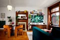 Cozy living room featuring orange velvet chairs, a round black table, a wooden mantel, and a large TV displaying green leaves.