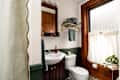 Small bathroom featuring a white sink, toilet, wooden accents, green trim, and a window with sheer curtains.