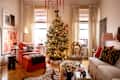 Cozy living room decorated for the holidays with a Christmas tree, orange armchair, and white sofa adorned with colorful pillows.