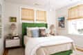 Bright bedroom featuring a green upholstered headboard, patterned pillows, a colorful lamp, and artwork on the walls.