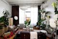 Cozy living room with a brown sofa, green plants, a round white pendant light, and a colorful rug.