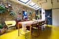 white dining room with one exposed brick wall and bright yellow floor
