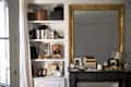 Stylish shelf with high heels, books, decorative boxes, and a large ornate mirror above a dark mantel with decor items.