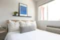 Cozy bedroom featuring a bed with striped pillows, a gray lumbar pillow, a plant, and a blue art print on the wall.