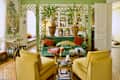 Bright living room featuring a green velvet sofa, yellow chairs, decorative plants, and unique art pieces.