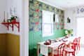 Bright dining area featuring a wooden table with red chairs, green wainscoting, and colorful floral wallpaper.