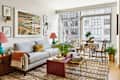 Bright living room featuring a patterned sofa, colorful artwork, and a small dining table with plants.
