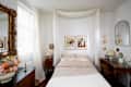 A bedroom featuring a bed with checkered bedding, framed art, a vintage mirror, and floral decor.