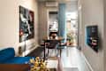 Cozy living space featuring a blue sofa, round dining table with fruit bowl, and a balcony with potted plants.