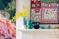 Colorful vases and a floral arrangement on a white mantel, with vibrant artwork in the background.