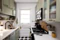 Compact kitchen with green cabinets, stainless steel appliances, a black faucet, and checkered floor tiles.