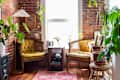 Cozy seating area with two yellow upholstered chairs, a round table, plants, and a brick wall backdrop.