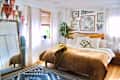 Cozy bedroom featuring a large bed with a brown quilt, decorative pillows, a patterned rug, and wall art.