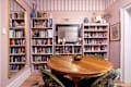 Cozy reading nook with a round wooden table, green upholstered chairs, and bookshelves filled with various books.