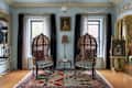 Two ornate chairs with striped cushions facing each other on a colorful rug, framed artwork, and a lamp in a bright room.