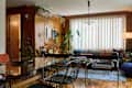 Modern living room and dining area with wooden accents, plants, glass table, and a blue sofa with colorful cushions.