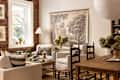 Cozy living room with exposed brick wall, white armchairs, a wooden table, and a large landscape artwork.