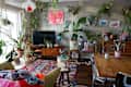 Colorful living room with plants, a TV, eclectic decor, a wooden dining table, and a vibrant rug.