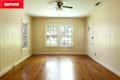 Empty room with light-colored wood paneling, two large windows, a ceiling fan, and a wooden floor.