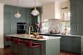 Modern kitchen featuring green cabinetry, marble countertops, brass fixtures, and red bar stools.