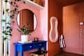 A vibrant entryway featuring a blue console table, round mirror, potted plant, and colorful walls.