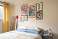 Cozy bedroom with a bed featuring blue and cream bedding, colorful wall art, a mirror, and a side table with decor.
