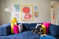 Cozy living room with a blue sofa, colorful pillows, a dog lounging, and vibrant wall art featuring food themes.