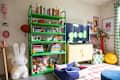 Colorful living room with a green bookshelf, plush toys, a yellow cabinet, and a blue pet bed.