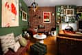 Cozy living room with green walls, brick accents, eclectic art, a white coffee table, and colorful textiles.