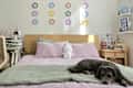 Cozy bedroom with a bed featuring lavender pillows, a green blanket, a plush bunny, and a dog resting on the bed.
