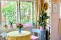Bright dining area with a round yellow-striped table, pink flower vase, and green plants by the window.
