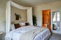 Cozy bedroom featuring a large bed with white linens, decorative pillows, and a plant, with an adjoining bathroom visible.