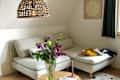 Cozy living area featuring a light gray sectional sofa, a vase of colorful flowers, a pink candle, and a wooden coffee table.