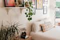 Cozy bedroom corner with a bed, decorative pillows, a plant, framed artwork, and a stylish lamp.