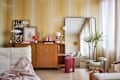 Cozy living room with a wooden sideboard, colorful decor, plants, and a large mirror reflecting natural light.