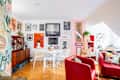 Bright living space featuring a round dining table with white chairs, red accent chairs, and a gallery wall of diverse artwork.